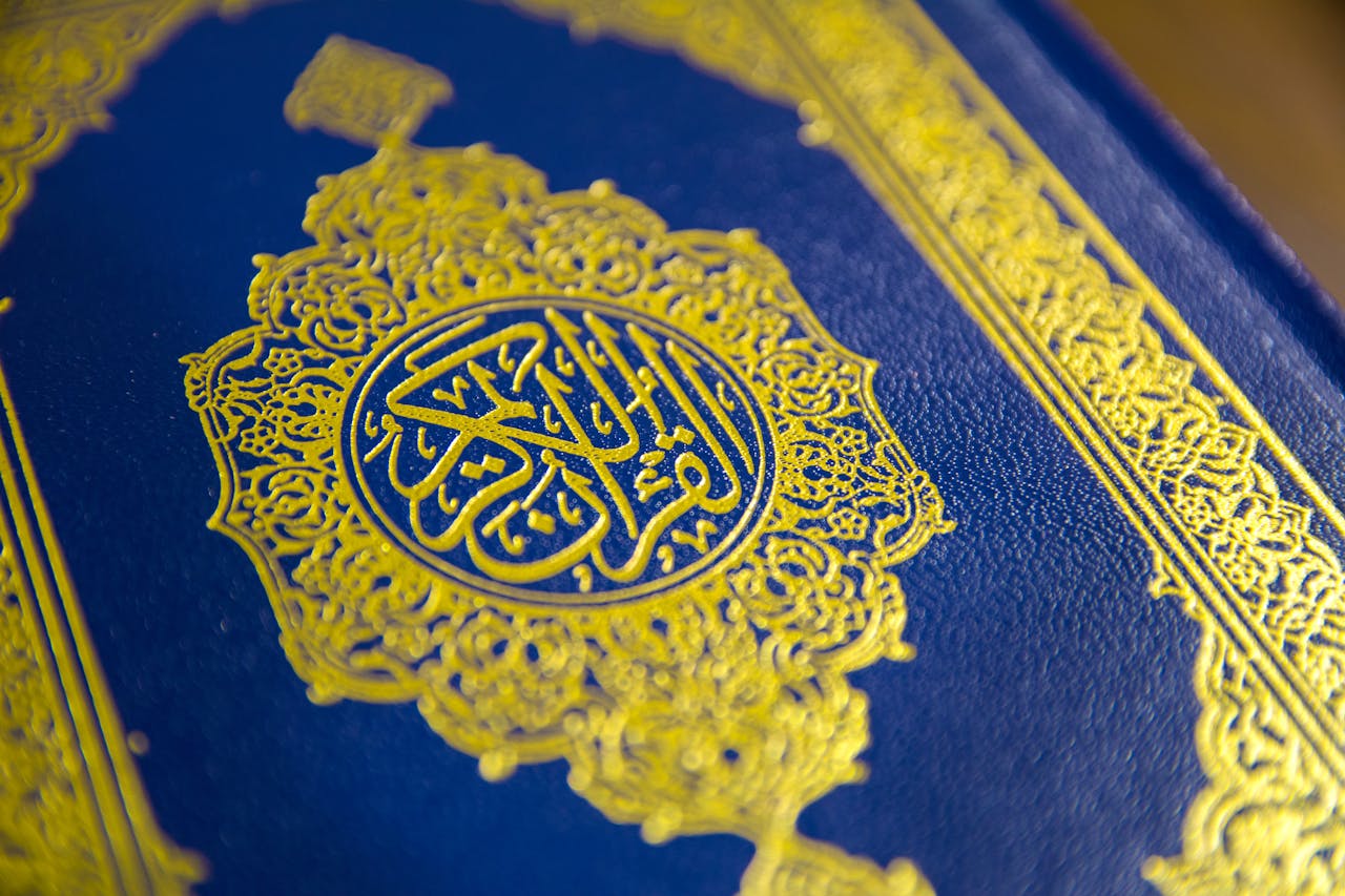 services-03 Close-up of intricate gold Quranic calligraphy on a blue cover, showcasing elegant Islamic design.