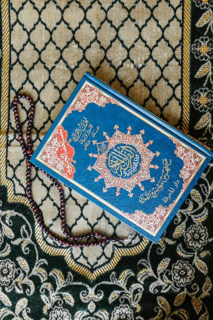 services-04 Top view of a Quran with prayer beads on a decorative Islamic carpet.
